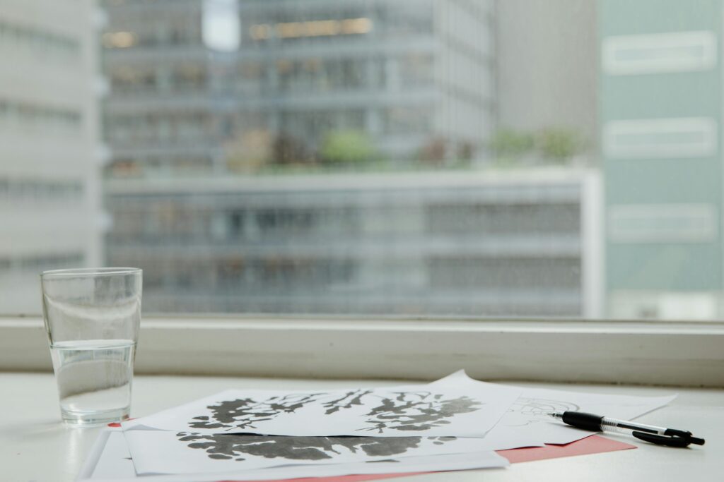 A minimalist office desk setup featuring psychological test papers, a glass of water, and a pen.